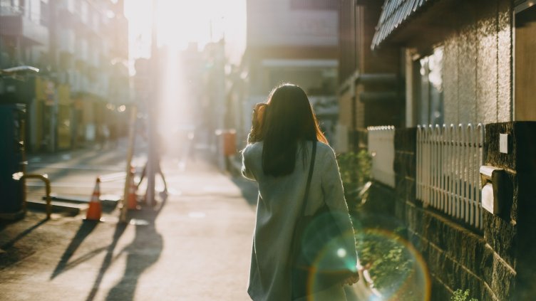 Rear view of woman leaving home to work in the early morning against warm sunlight