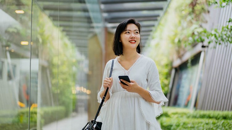 a smiling woman holding smartphone and looking away in a green building