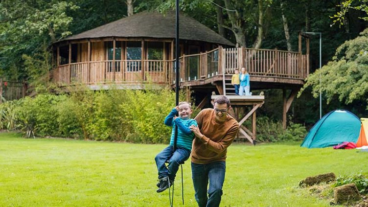 A father is playing with his kid in garden(his wife and daughter behind him)