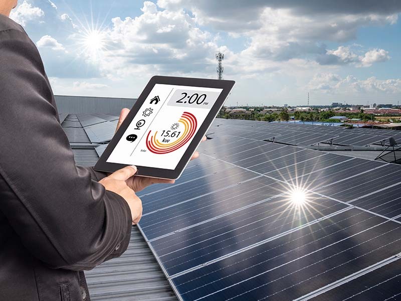 Man examining generation of solar power plant, holding digital tablet with a chart of electricity production.