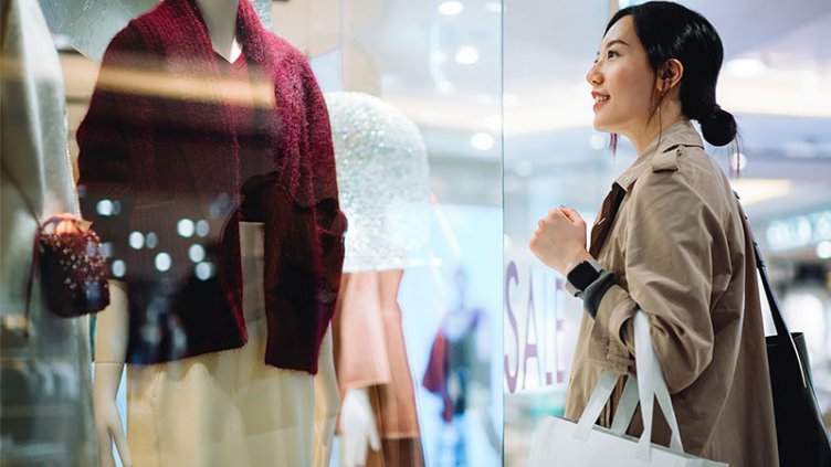 Woman looking at clothes through glass window at shopping center