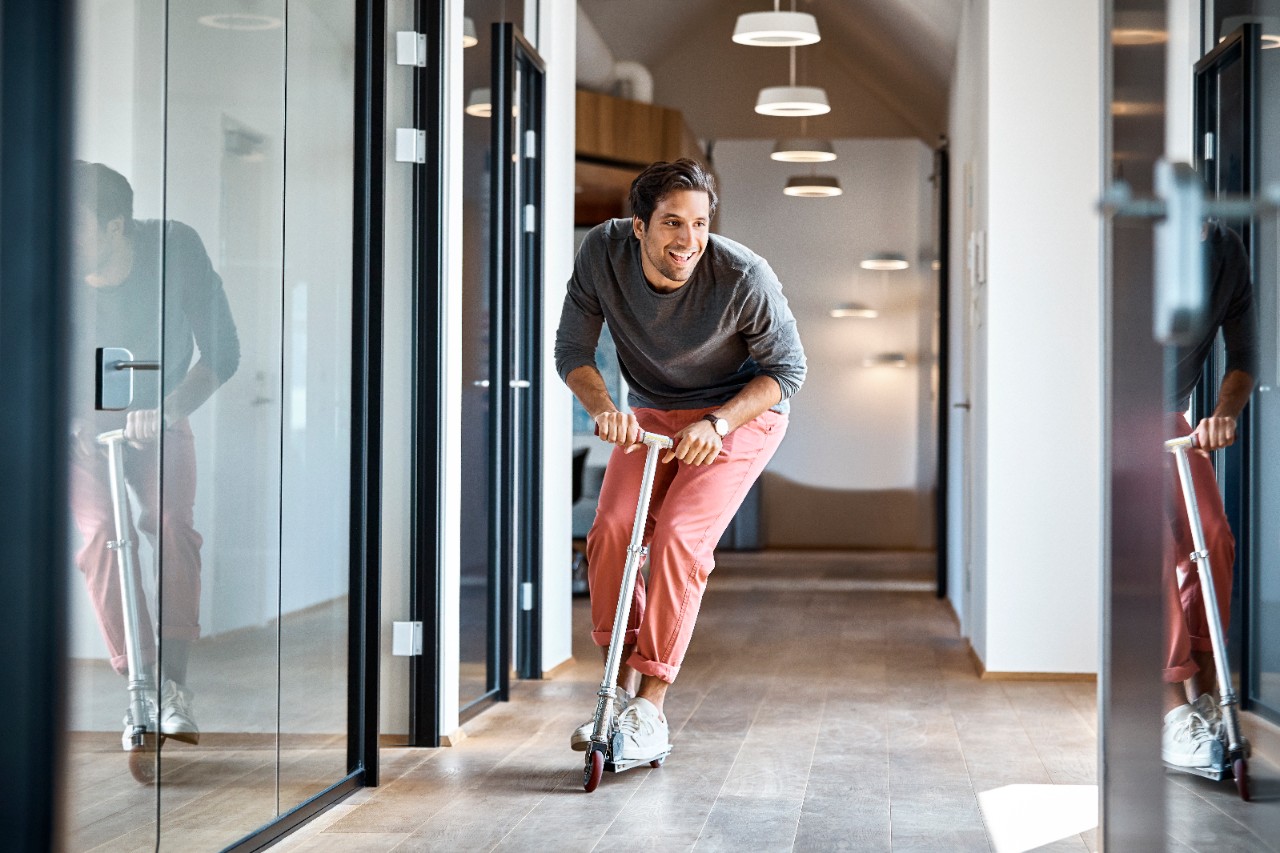 Happy young businessman enjoying while riding push scooter in office corridor