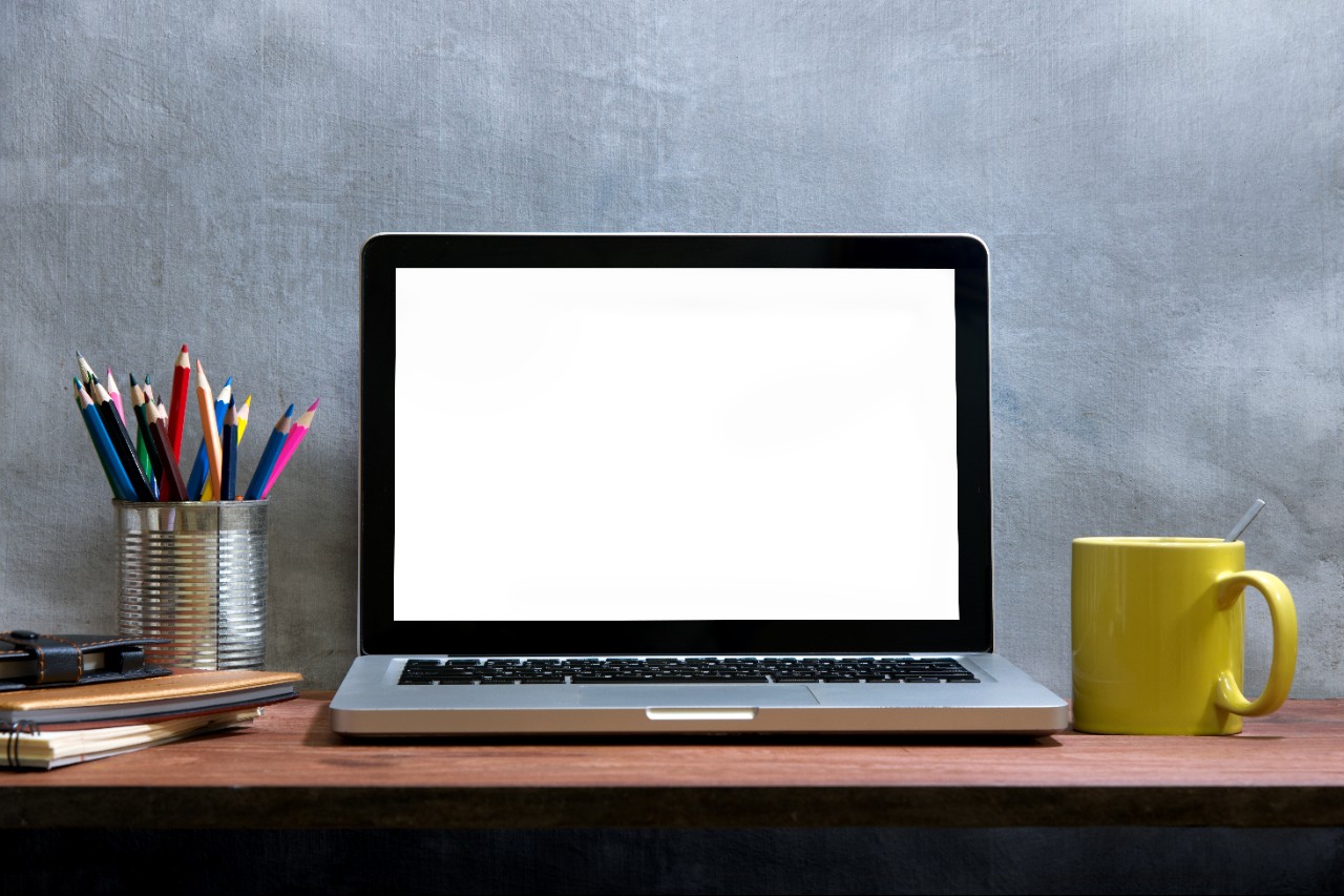 Blank laptop screen with books, colored pencil and cup of coffee on wooden table